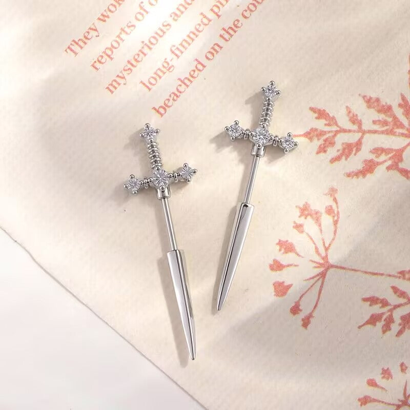 Pair of silver dagger sword stud earrings paved with clear zircon crystals on a vintage paper background.
