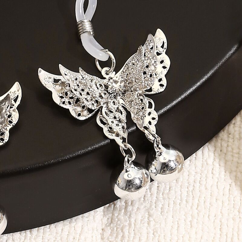 Detailed close-up of an intricate filigree butterfly body jewelry piece featuring two polished metal bells.