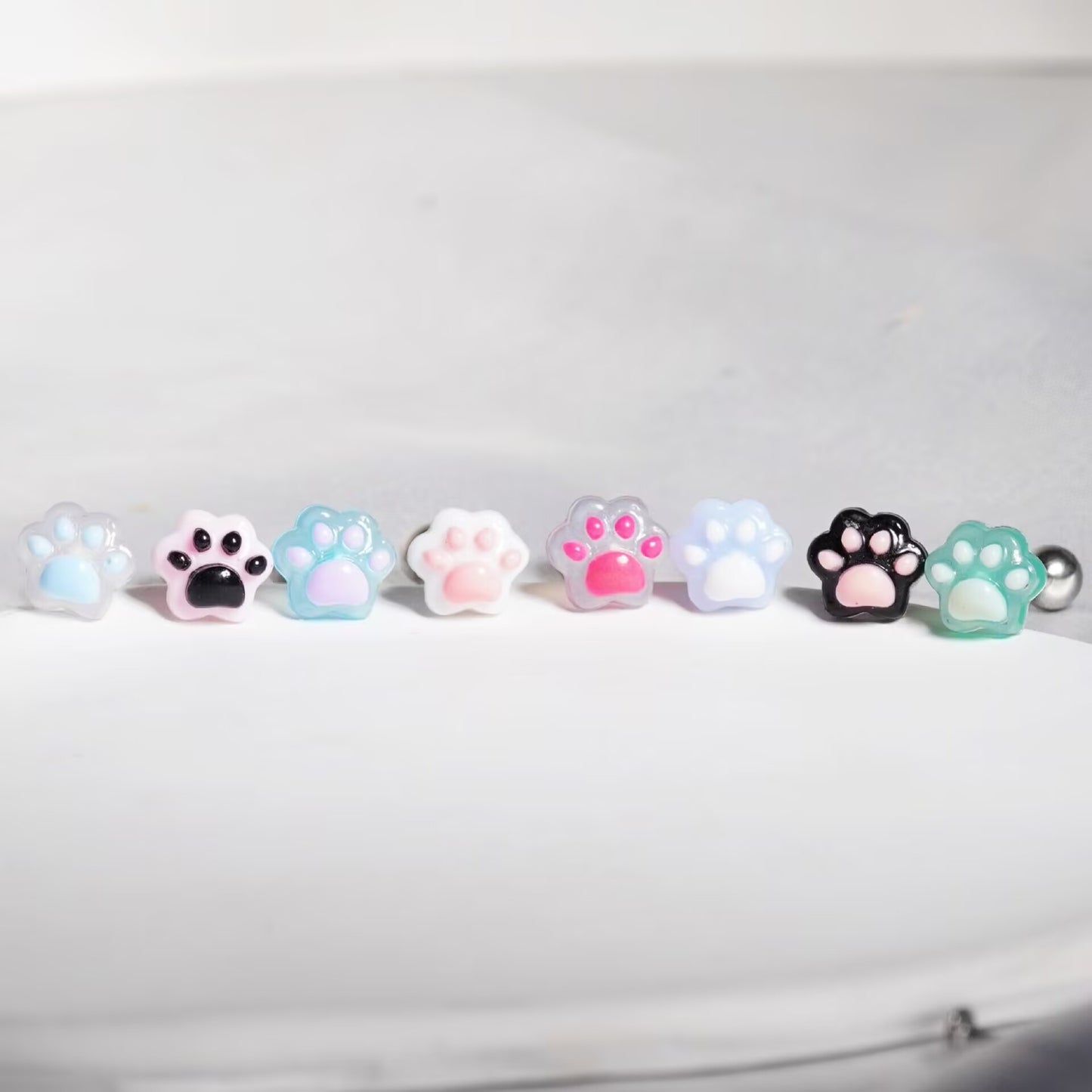 Lineup of cute resin cat paw tongue rings showing 8 color variations including pink, black, blue, and purple