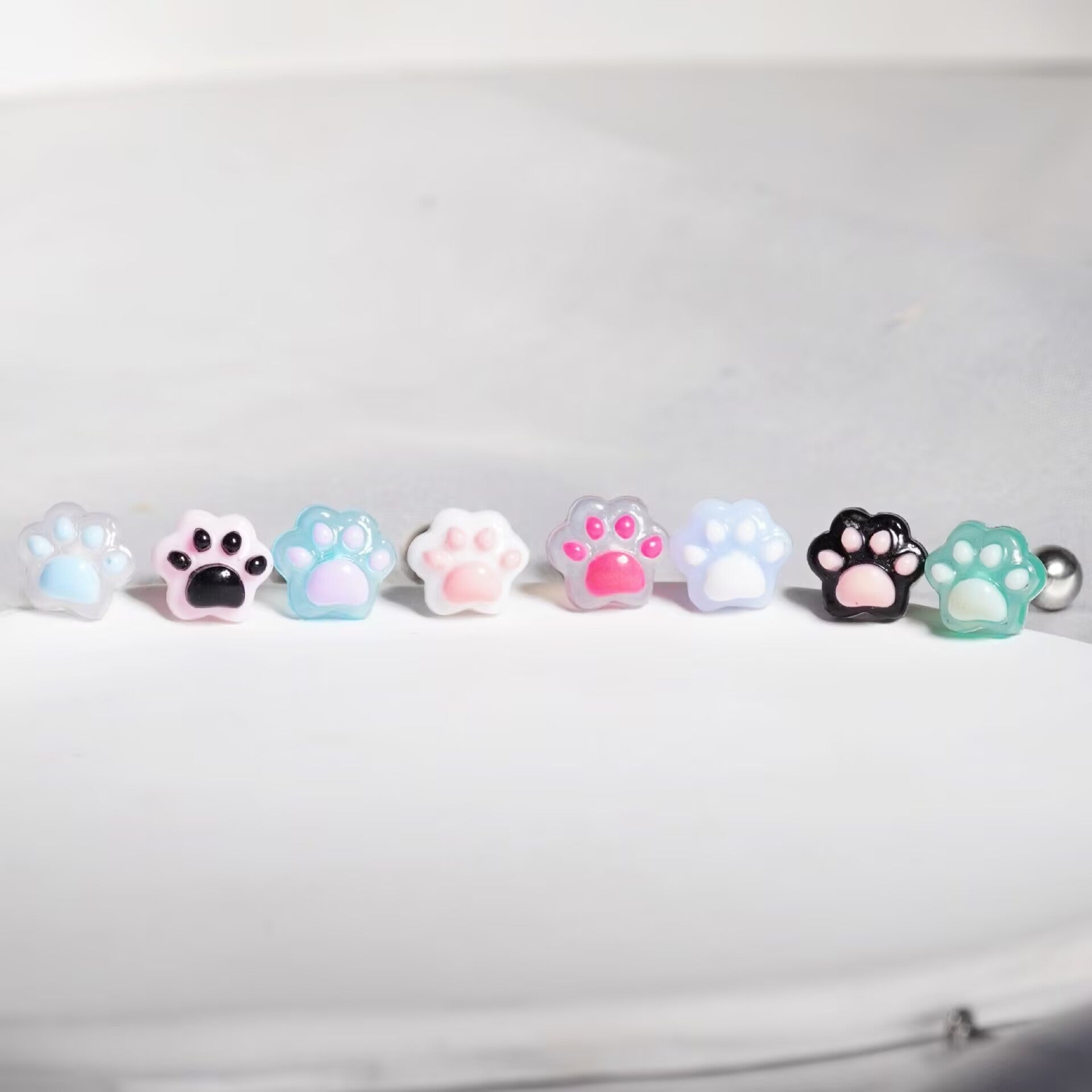 Lineup of cute resin cat paw tongue rings showing 8 color variations including pink, black, blue, and purple
