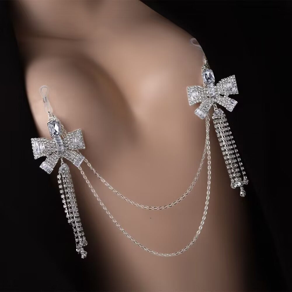 Close up shot of a person wearing a single silver Coquette rhinestone bowknot non piercing nipple clasp chain featuring interconnected dual bowknots and cascading crystal tassels.