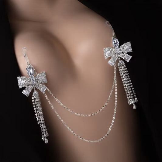Close up shot of a person wearing a single silver Coquette rhinestone bowknot non piercing nipple clasp chain featuring interconnected dual bowknots and cascading crystal tassels.