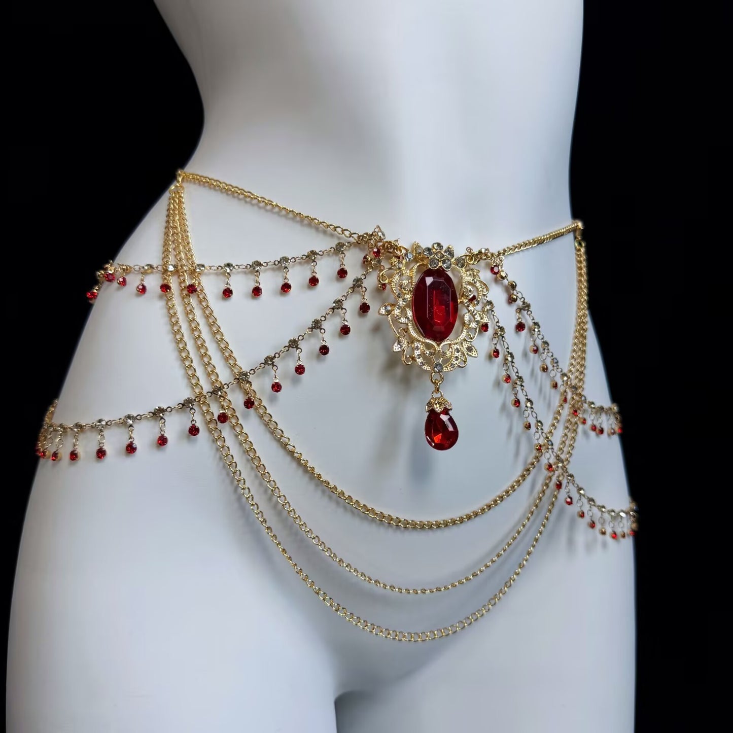 Detailed view of a luxury multi-tier gold waist chain featuring a large crimson ruby pendant, filigree border, and cascading red glass beads.