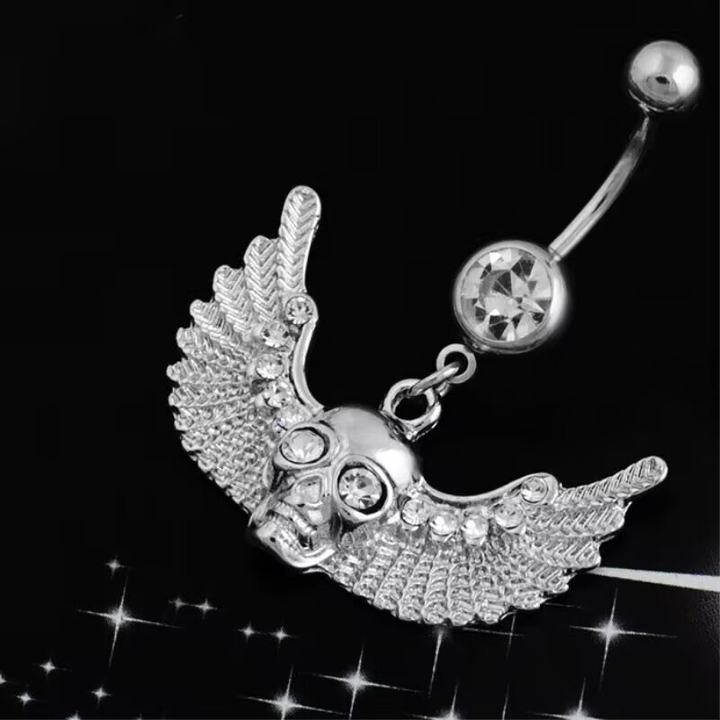 Side angled view showing the smooth curved barbell and crystal-encrusted winged skull navel piercing pendant.