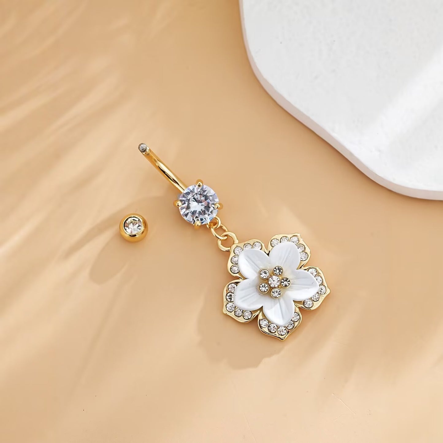 Close-up of a dainty flower dangle belly ring with an uncrewed top ball on a neutral background.