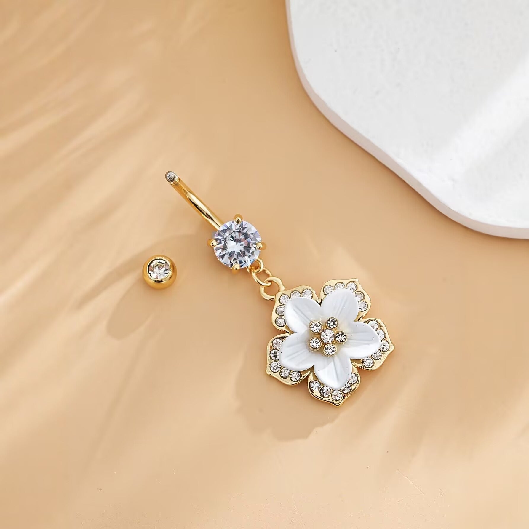 Close-up of a dainty flower dangle belly ring with an uncrewed top ball on a neutral background.