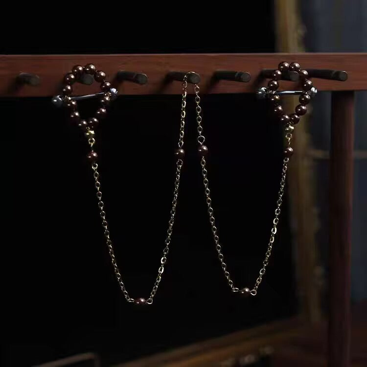 A detailed display of dark bronze coffee pearl nipple jewelry with a connected gold-tone body chain on a wooden rack.