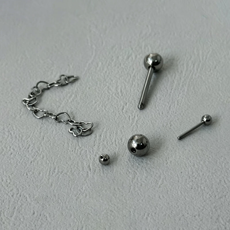 Fully disassembled cross tongue ring showing straight barbells, steel balls, and heart chain