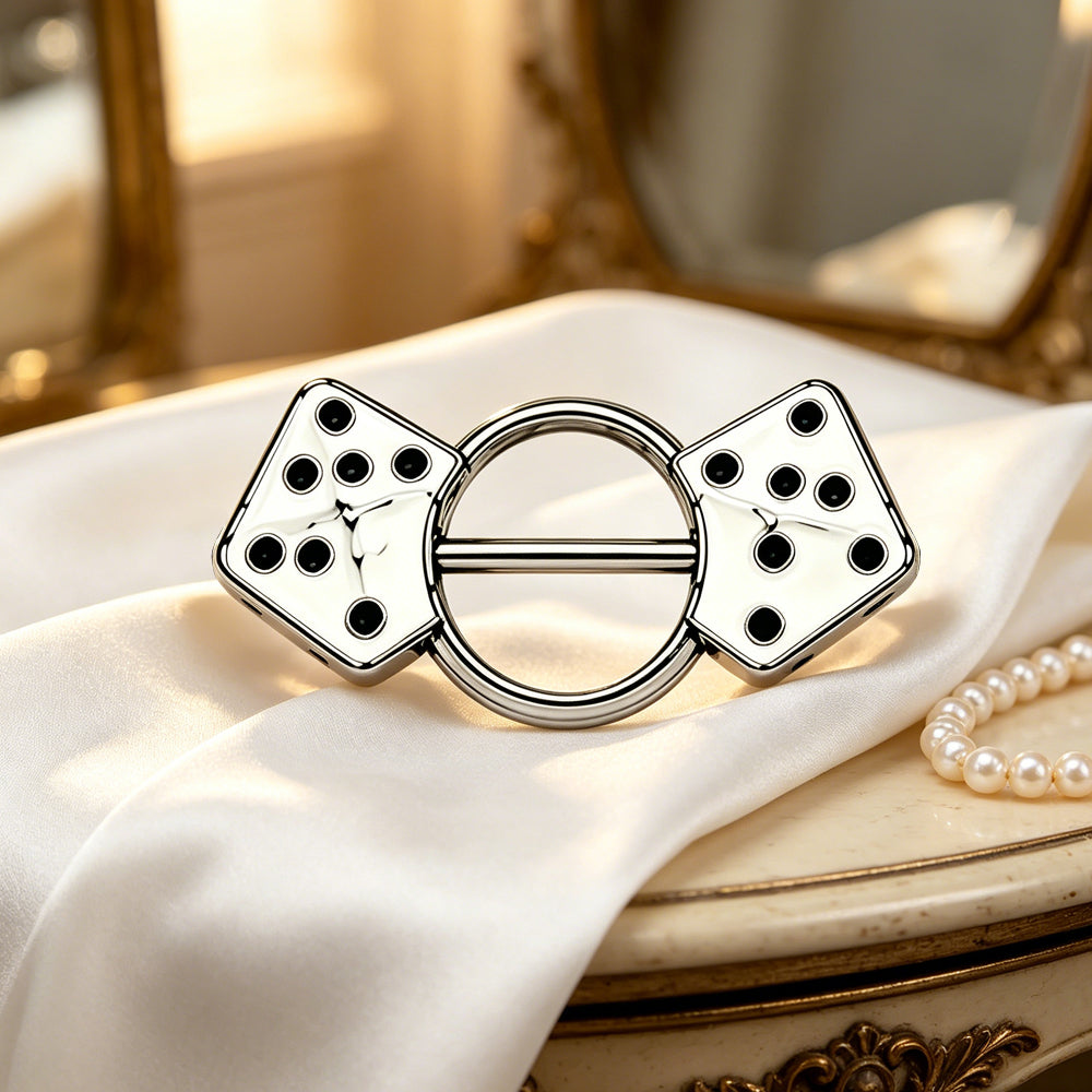 Aesthetic display of a dice nipple shield on white silk with pearls and a vintage mirror.