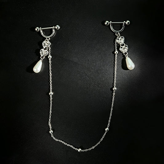 Front view of a one-piece integrated body jewelry set featuring double barbell rings connected by a long drape chain with heart shapes and teardrop pendants on a dark background.