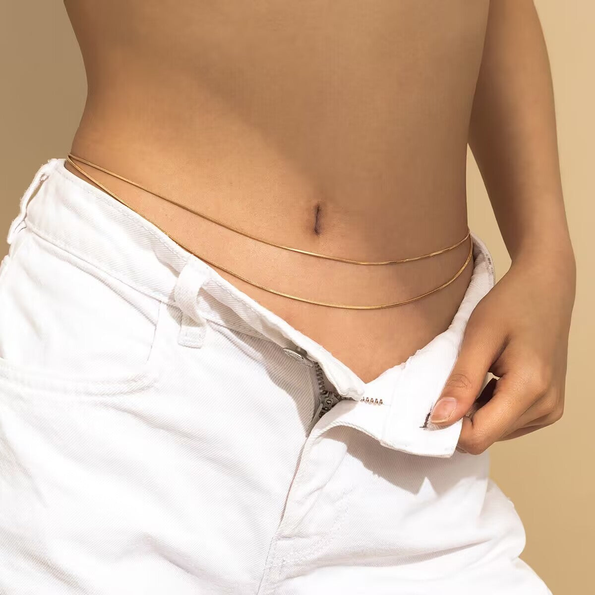 Model wearing a double-strand gold waist chain with unbuttoned low-rise white denim jeans.