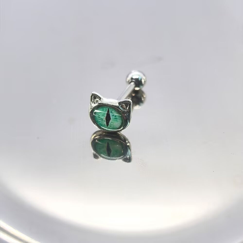 Emerald green cat eye tongue ring barbell with vertical pupil and cat ear frame resting on a polished silver mirror surface.