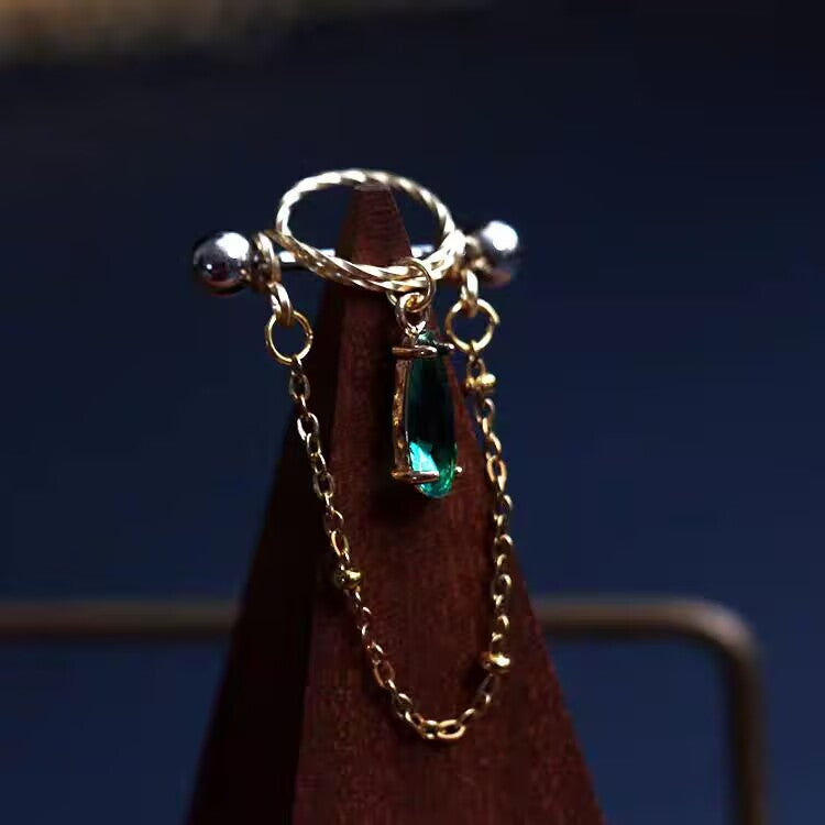 Emerald green waterdrop cubic zirconia nipple shield jewelry with gold draping chain on display mount.
