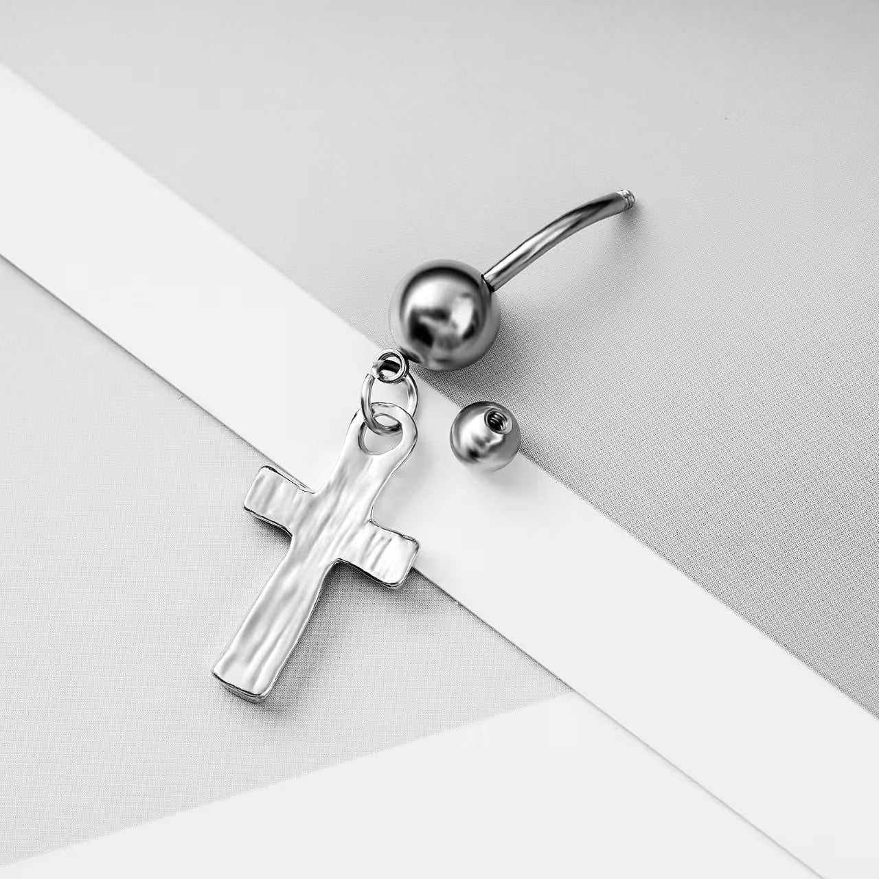 Close-up of the smooth metal texture and the unscrewed 5mm top ball showing the barbell of the cross belly ring.