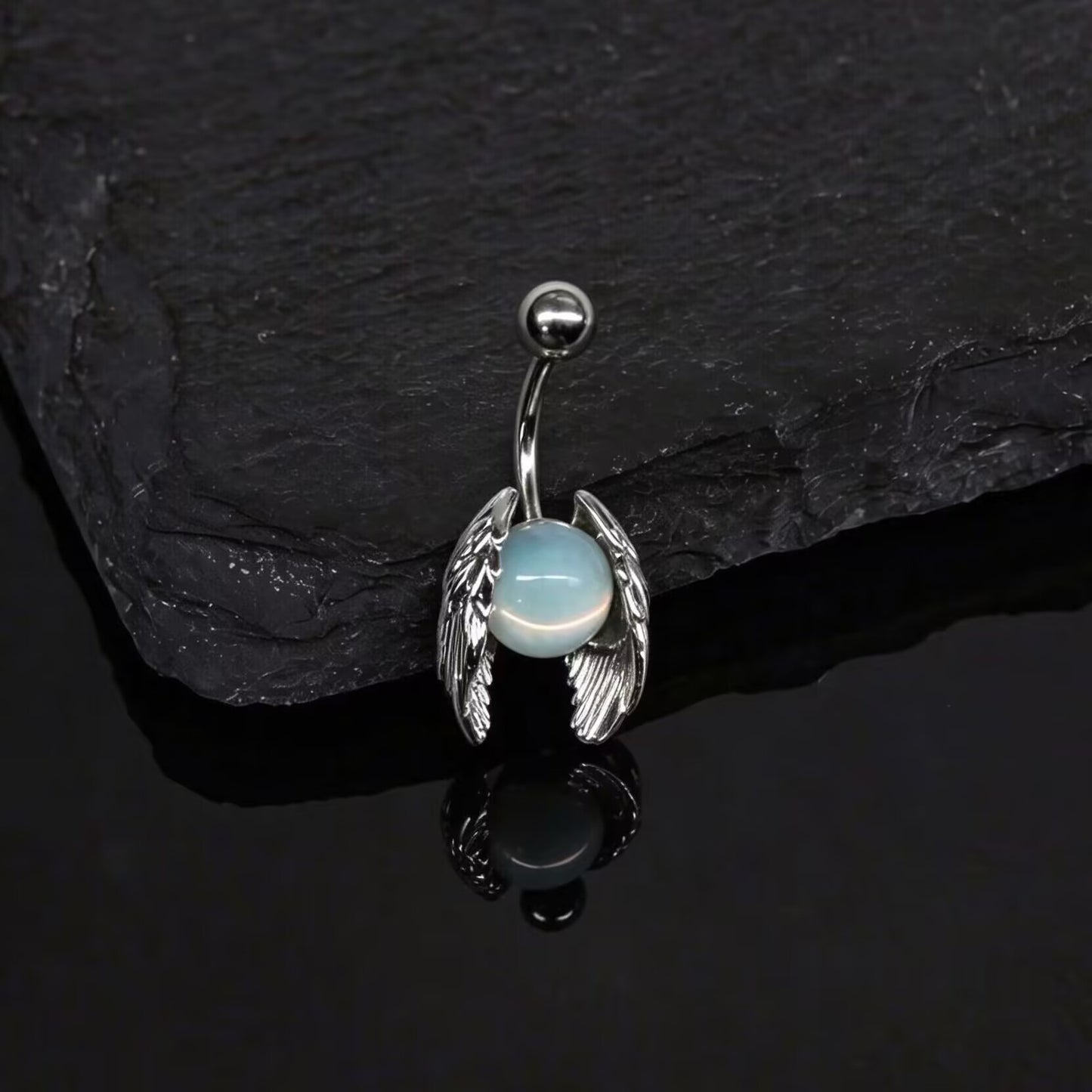 Fairycore blue opalite navel ring resting on a dark slate stone with soft lighting