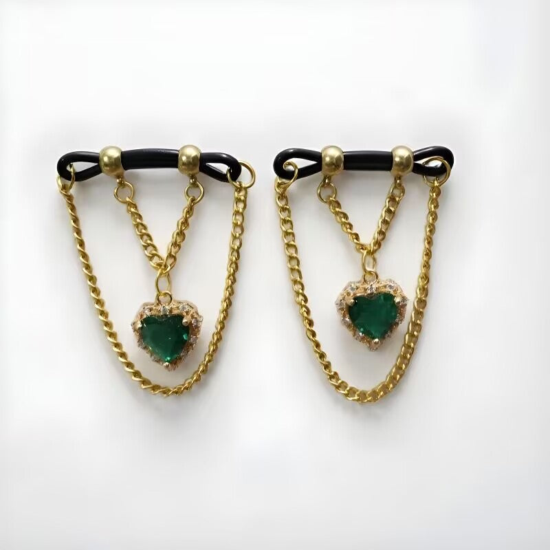 Fake nipple clamps set with emerald green heart cubic zirconia charms and hanging gold drop chains for non-pierced body decoration.