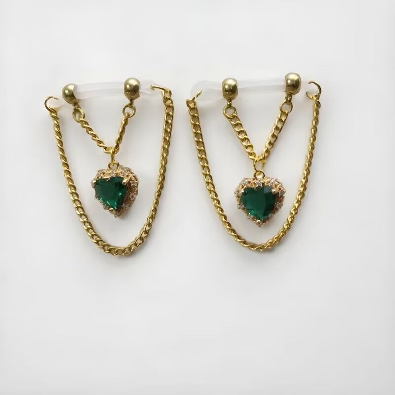 Fake nipple clamps pair designed with emerald green heart crystals and layered gold chains on clear adjustable loops.