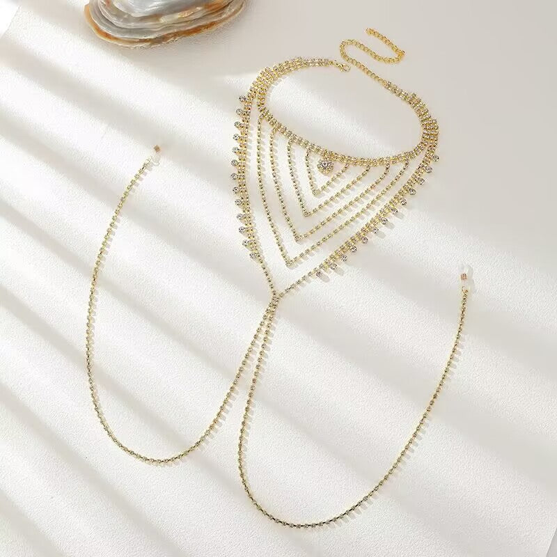 Side angle view of a gold crystal intimate body jewelry chain layout on a textured surface.