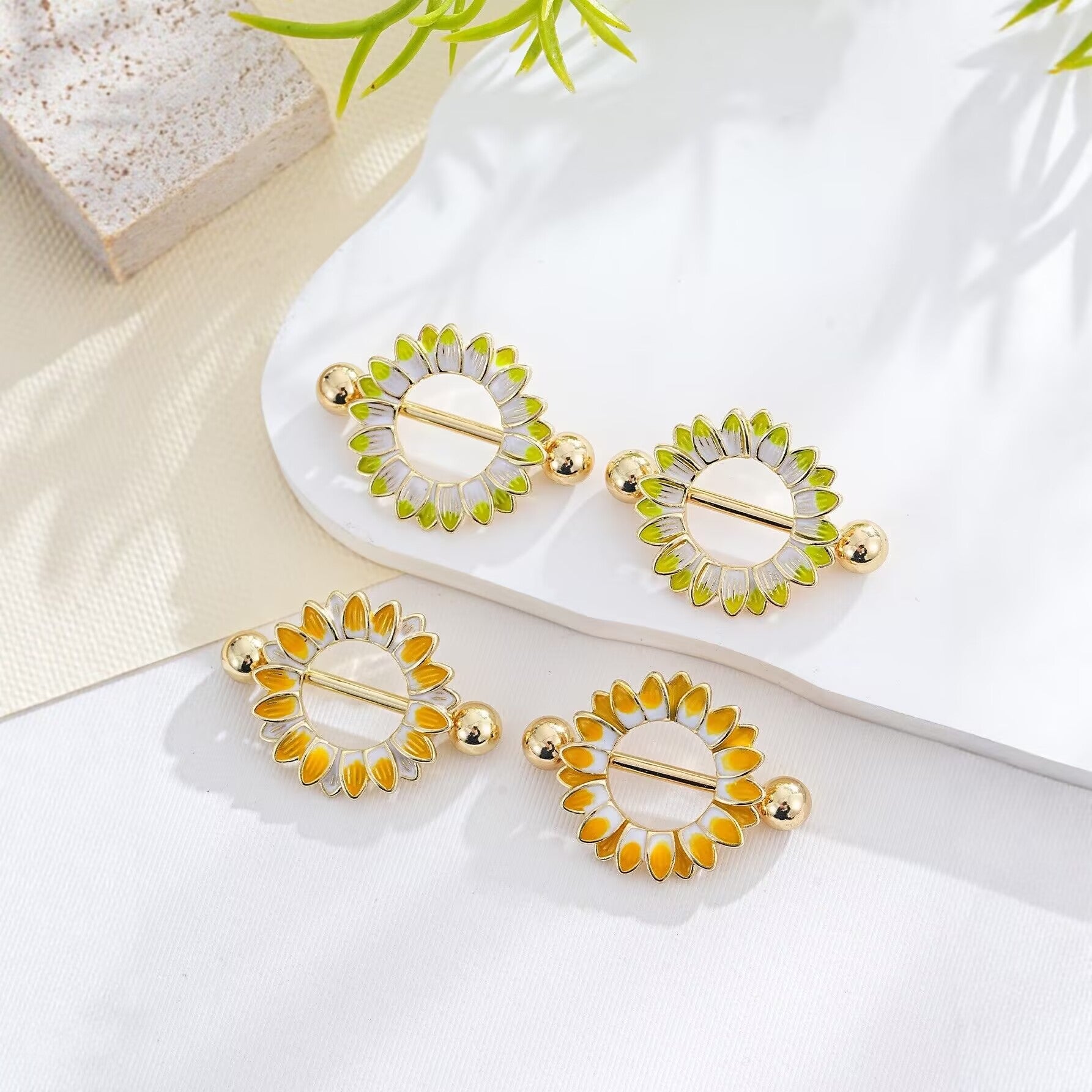 Multiple colors of sunflower nipple piercings arranged on a minimalist aesthetic prop.