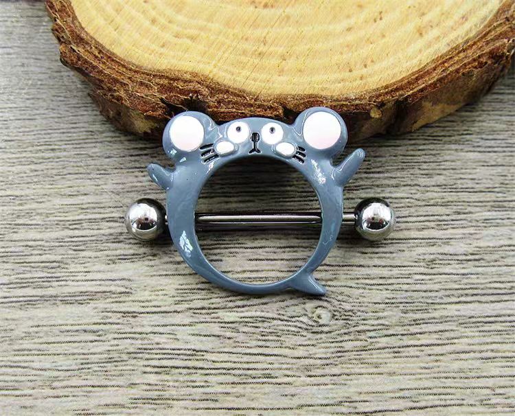 Real-life product shot of the funny mouse nipple piercing jewelry resting on a rustic wooden background, showcasing the glossy enamel finish.