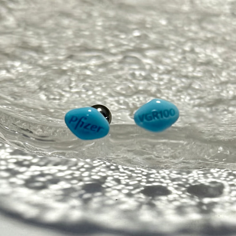 Funny blue pill body piercing jewelry displayed on a textured glass surface