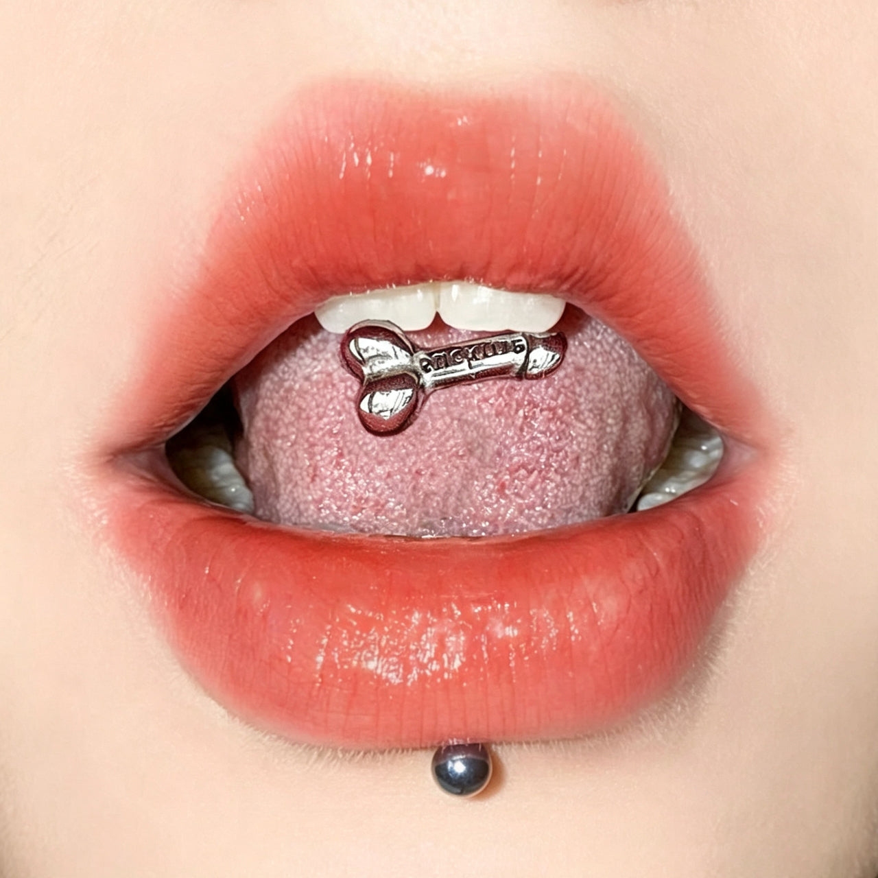 A person wearing a novelty penis-shaped tongue ring with an engraved suck me quote on the top barbell end.