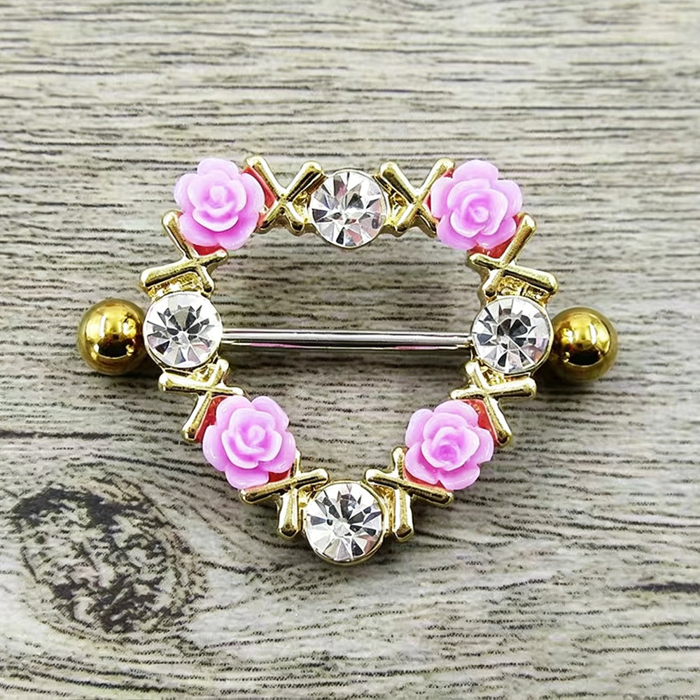Detailed macro shot of a gold-colored romantic alternative heart nipple shield ring with pink roses on a textured wooden background.