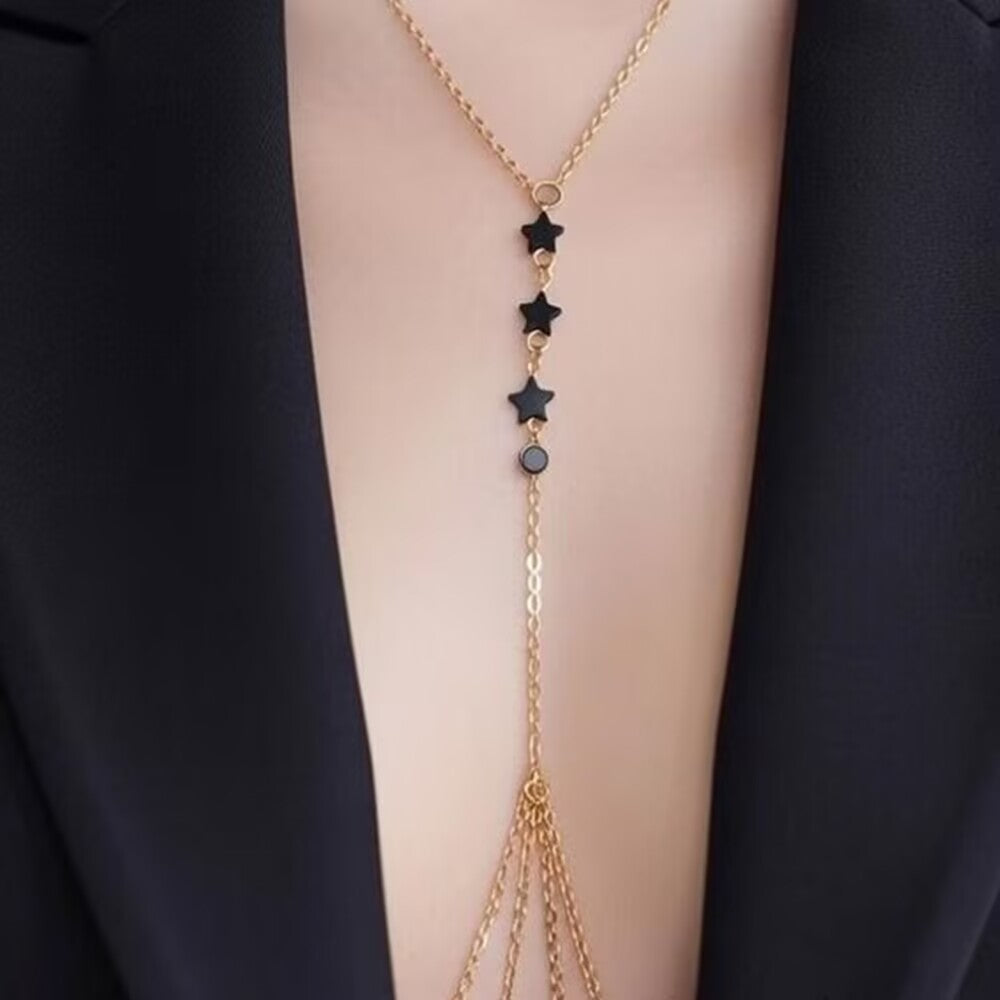 Woman wearing gold chest chain harness body jewelry over a black top.