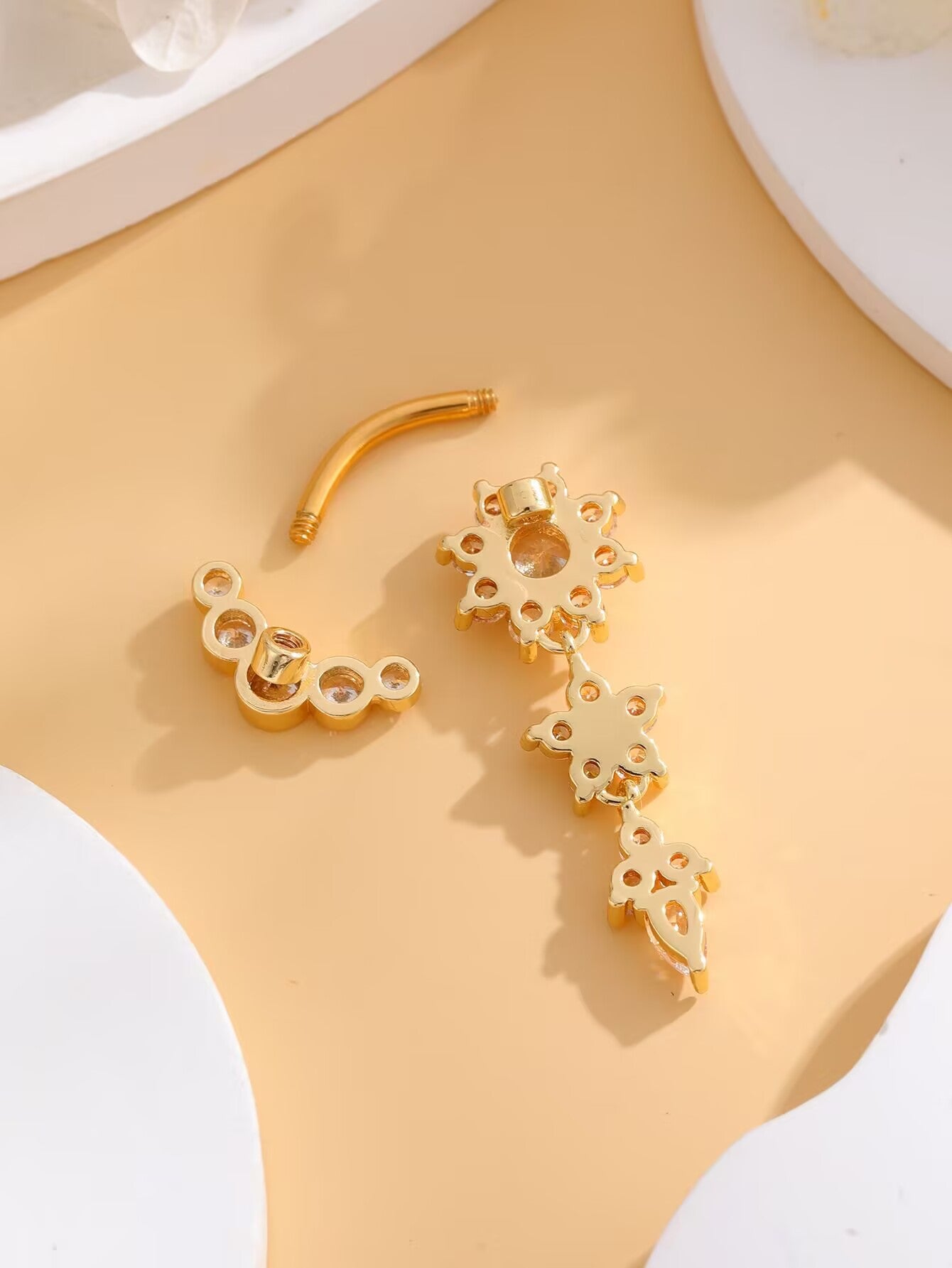 Gold curved barbell belly ring disassembled displaying threaded top closure and multi-layer dangle.
