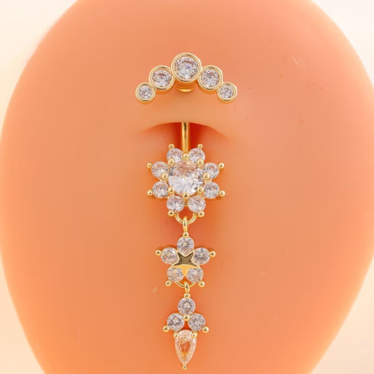 Gold dangle navel ring with flower pendant shown on piercing model for body jewelry styling inspiration.