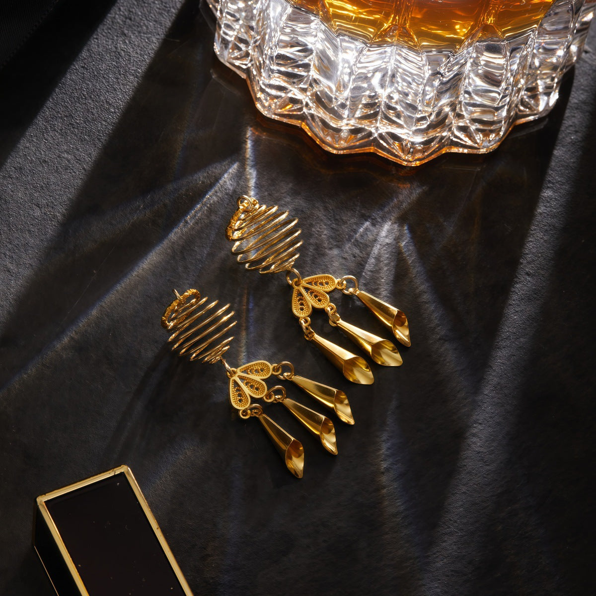 Gold taper dangle nipple jewelry displayed on a dark textured surface with luxury lighting.