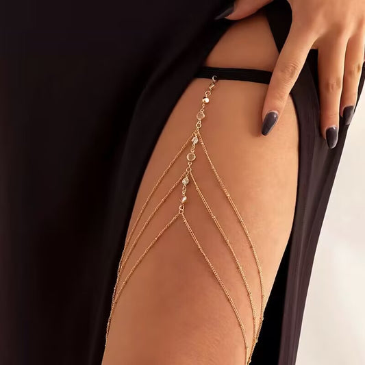 Gold layered rhinestone thigh chain body jewelry with elastic band worn on model with black dress