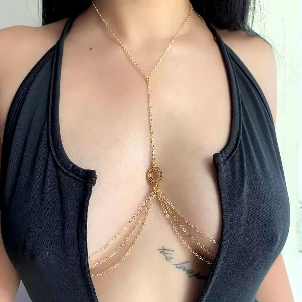Close-up of a woman wearing a gold non-pierced nipple chain body jewelry with multi-layer tassel harness design over a black open halter top, showcasing fake piercing sex appeal.
