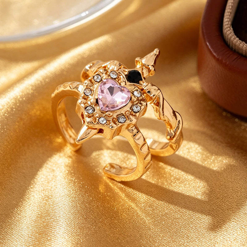 Gold-tone pink heart and black-accent sword open rings overlapping on gold fabric