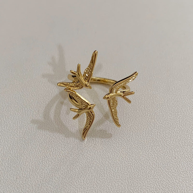 One gold-plated three-swallow ring showing sculpted wings, feather details and the ring band.