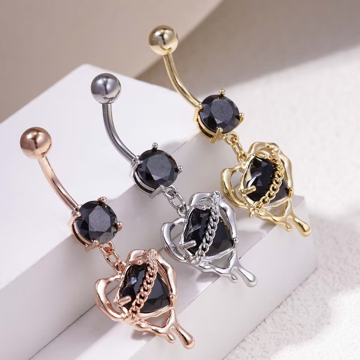 Gold, silver, and rose gold liquid lava black heart dangle belly button rings displayed side by side