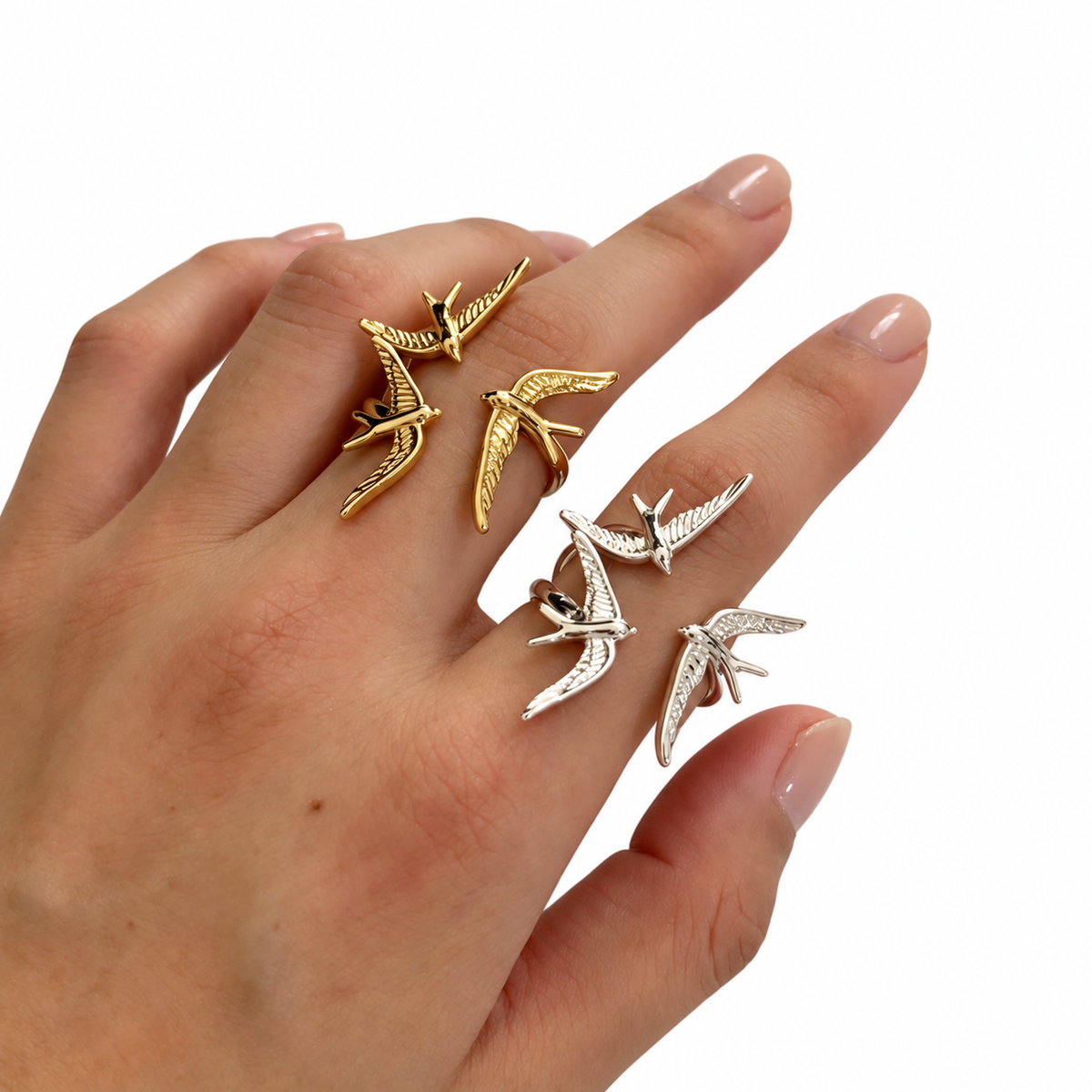 Gold and silver-tone three-swallow statement rings worn on adjacent fingers.