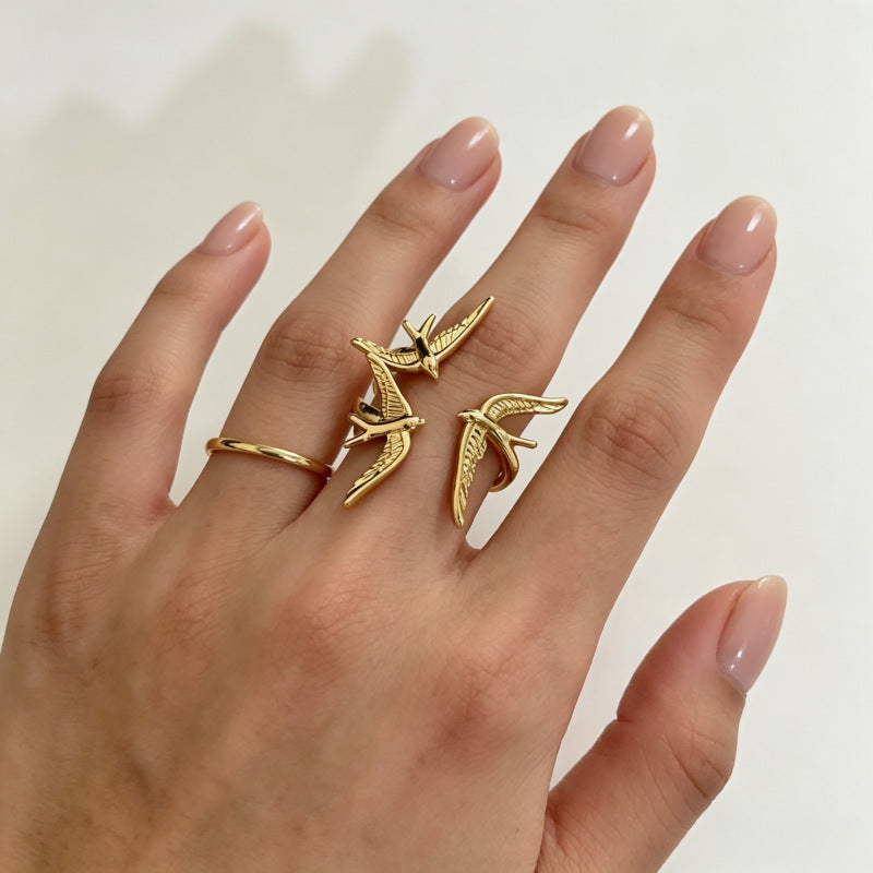 One gold three-swallow statement ring worn beside a plain gold band.