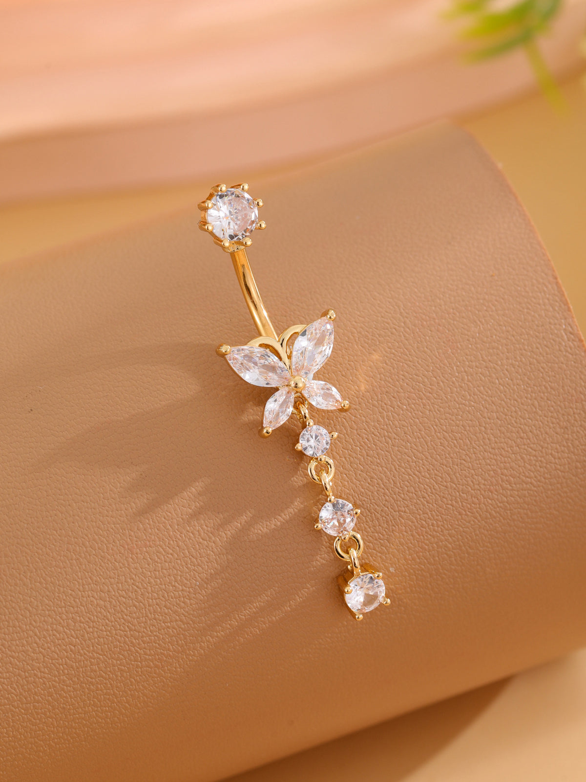 Single gold-tone butterfly cubic zirconia navel ring angled on tan display