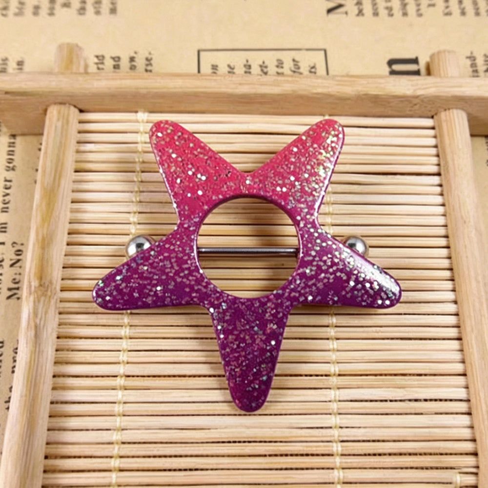 Aesthetic close-up of an alternative style glitter star nipple shield resting on a bamboo mat with a vintage newspaper background, showcasing the glossy pink and purple texture.