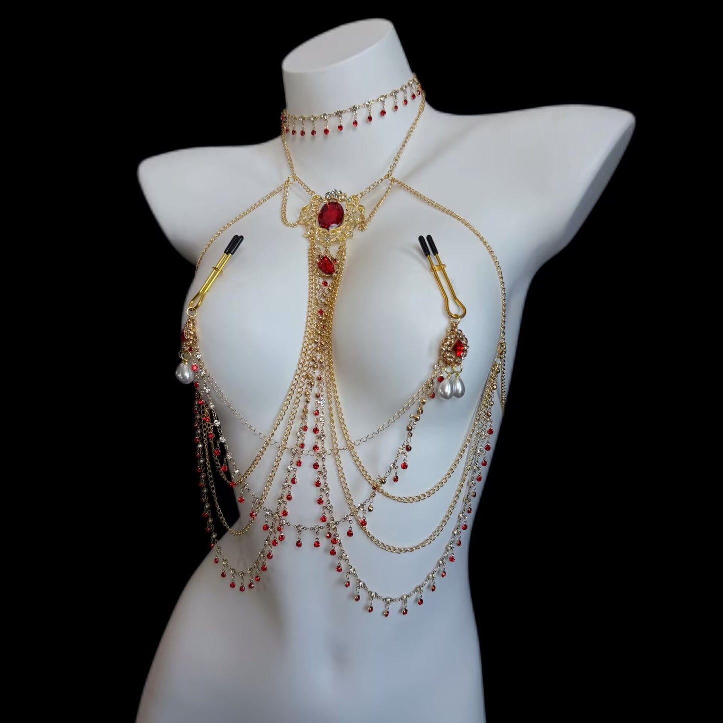 Gothic style gold chest harness body chain paired with black rubber-tipped U-shaped breast clips, ruby drop beads, and dangling pearl charms on mannequin.