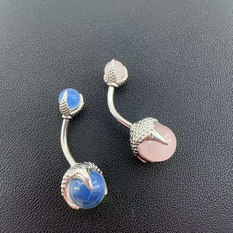 Two gothic dragon claw navel rings side by side showing blue and pink polished spheres on a dark background.