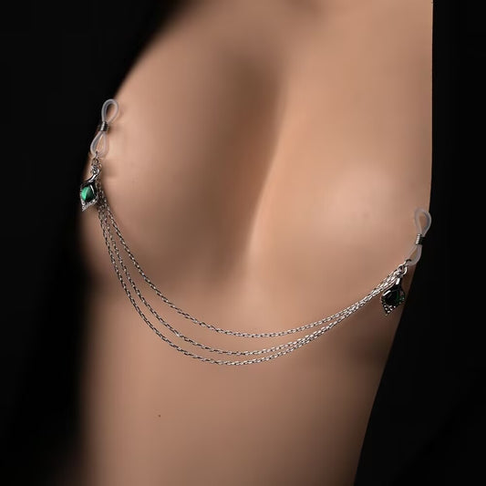A close-up of a model wearing a silver multi-layer non-piercing nipple body chain with green emerald charms connected across the chest.