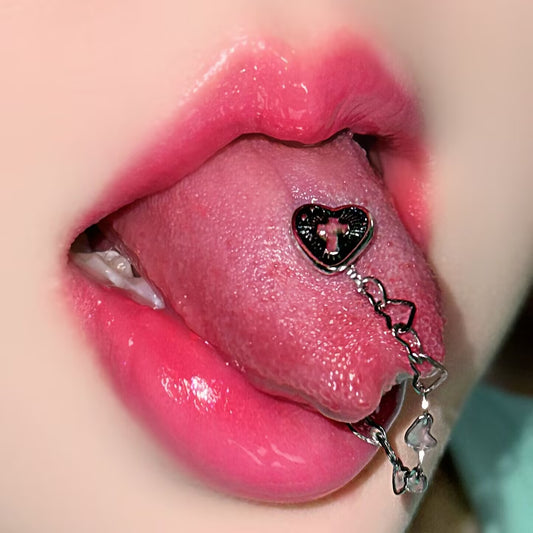 Close-up shot of a model wearing a gothic heart cross tongue ring with a dangle heart chain for Y2K alt fashion.