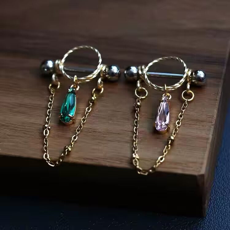 Green and pink pear-cut CZ nipple shield barbells displayed side by side on wooden block.