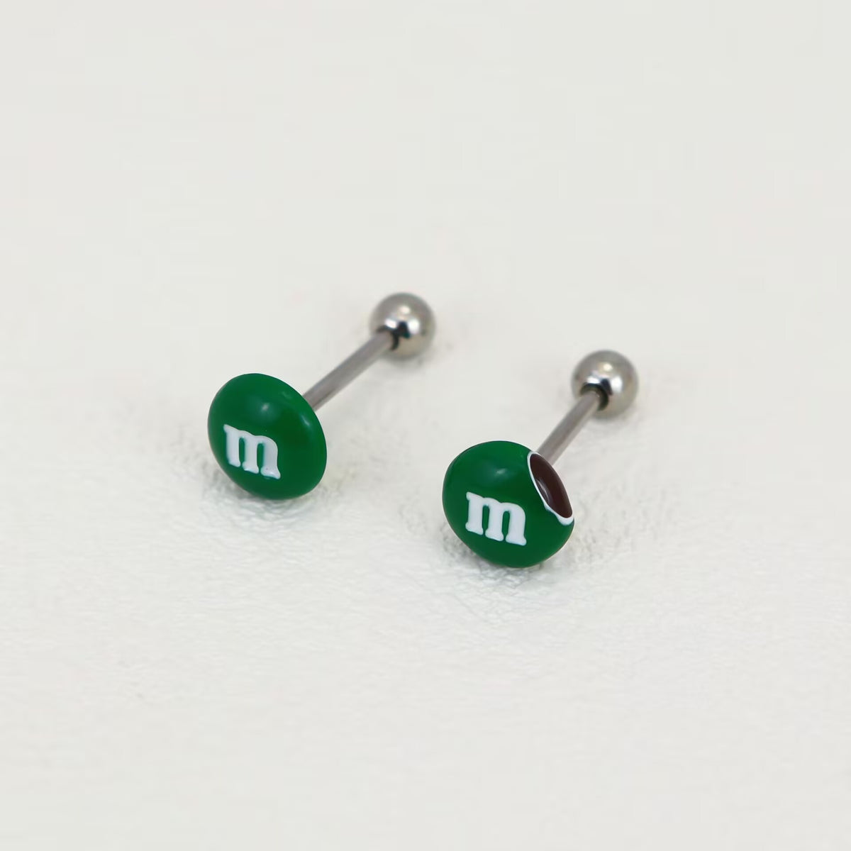 Pair of forest green M&M candy tongue rings showing both complete and bitten styles side by side.