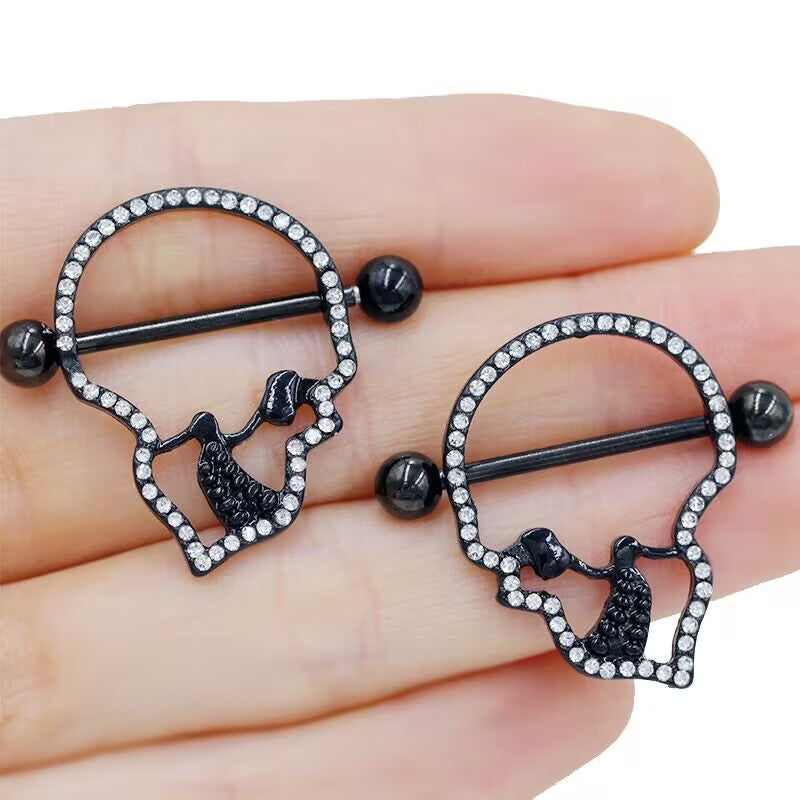 A pair of black skull nipple rings held in hand to show real-life scale.