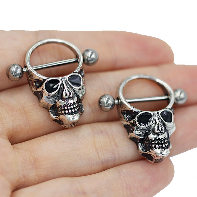 Close-up view of a person holding two skull nipple rings with dark oxidization for a vintage look