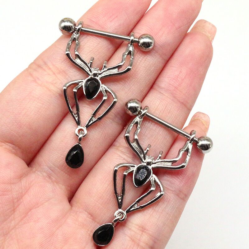 Two spider-shaped nipple shield jewelry pieces held in a hand to show scale and detail.