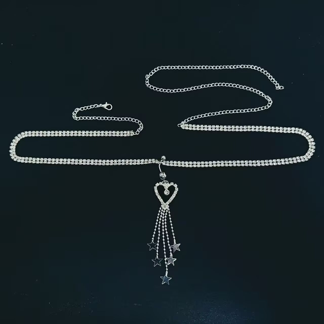 Flatlay of dangling heart shaped belly button ring with star tassel waist chain body jewelry.
